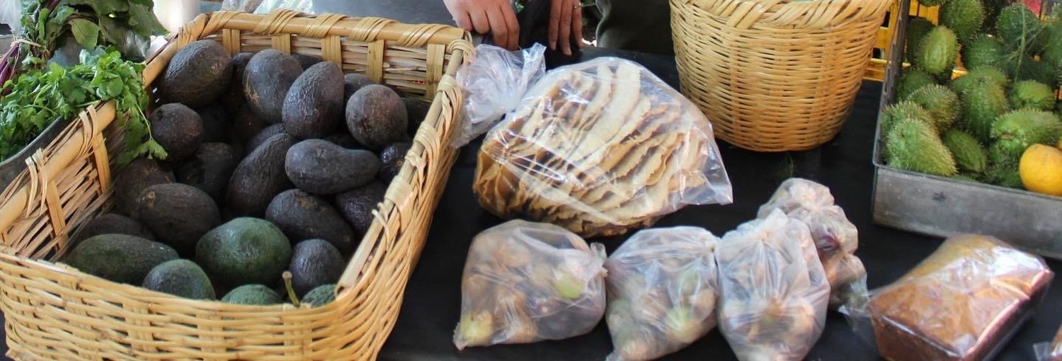 Canastas de aguacate y tortillas hechas a mano en el puesto de Acampo, con guanábanas al fondo