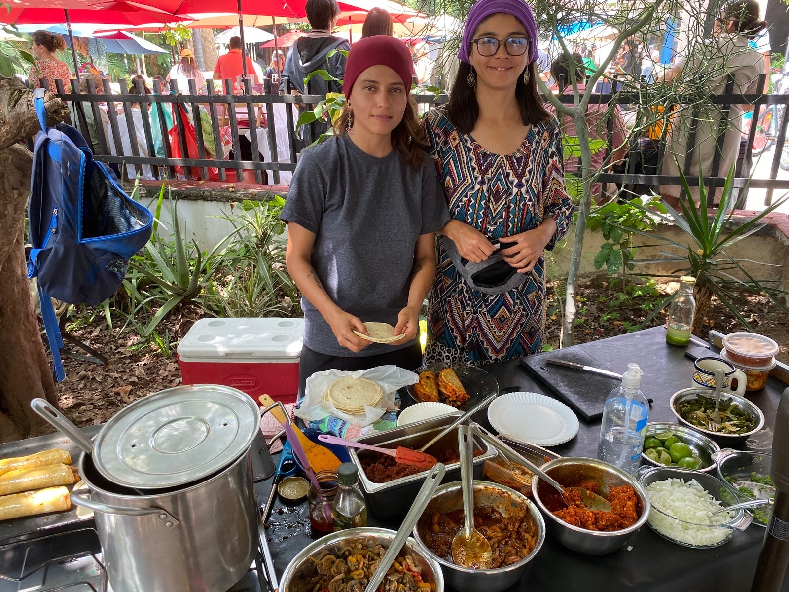 Dos integrantes de Ajodisiaca preparando tacos en su puesto, rodeadas de ollas y guisos