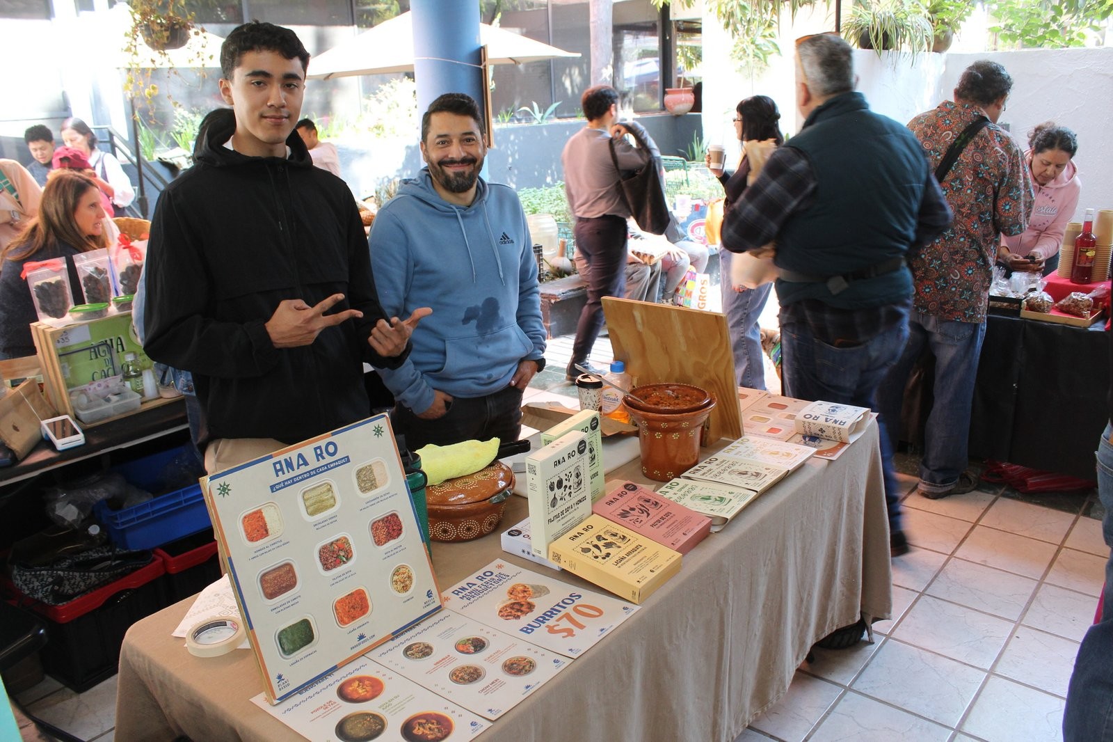 Equipo de Ana Ro en su puesto, con el póster del menú y los empaques de producto sobre la mesa