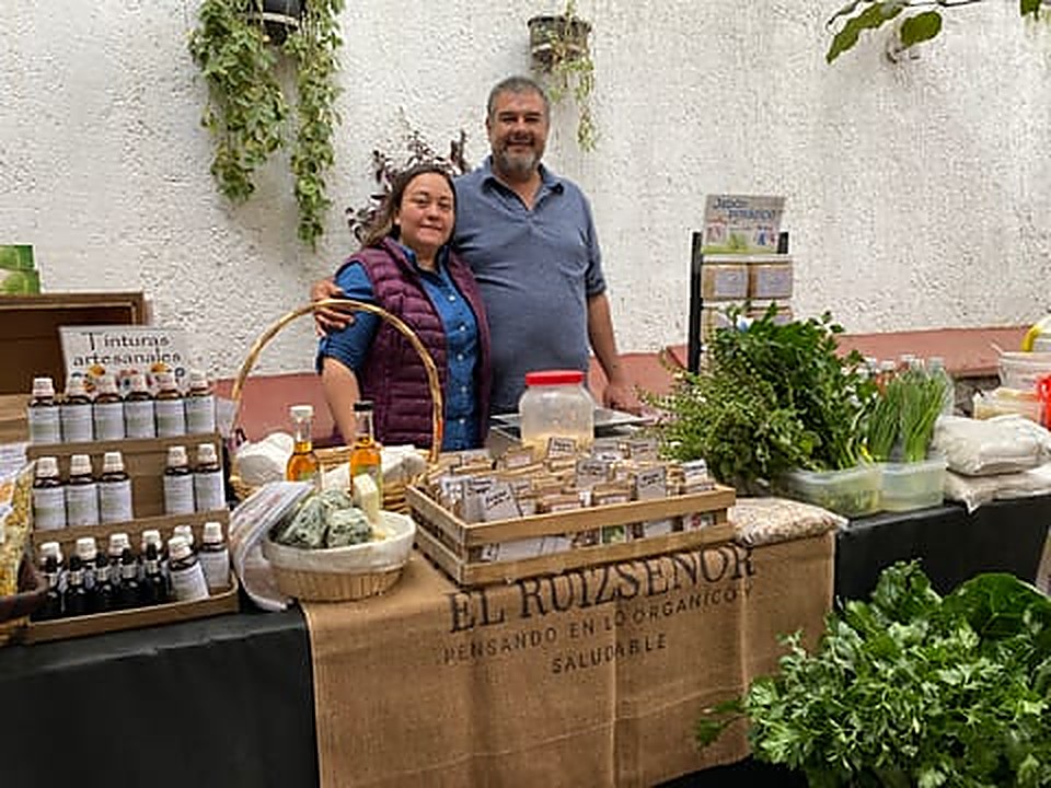 Puesto de Granja El Ruizseñor con hileras de tinturas artesanales, hierbas frescas y el letrero de yute de la marca
