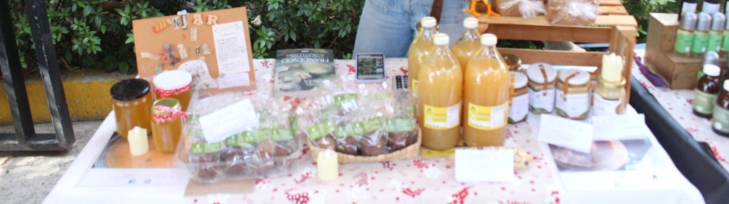 Pan artesanal, jugo embotellado, miel y tsampas de Manjar de Vida, exhibidos sobre la mesa del puesto