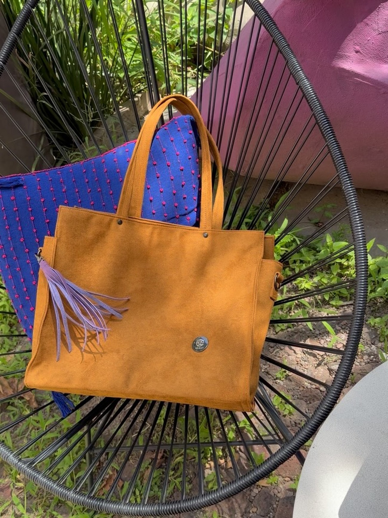 Bolsa tote color mostaza de Munay, con dije de borlas, sobre una silla Acapulco