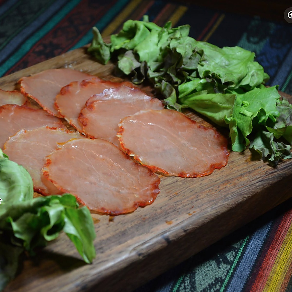 Rebanadas de charcutería curada sobre una tabla de madera, junto a hojas de lechuga
