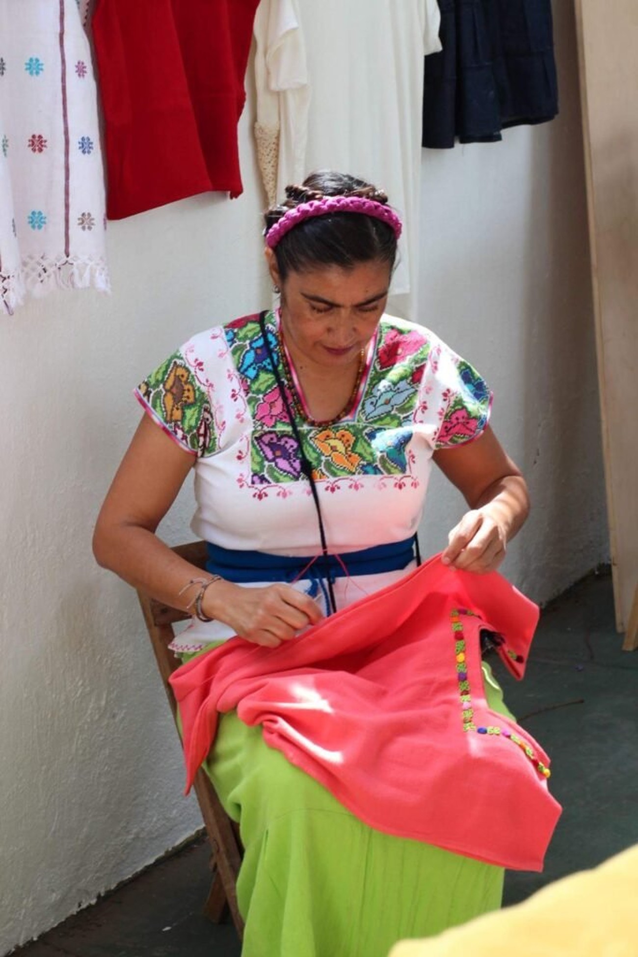 Artesana bordando a mano una prenda roja de Pies de Barro, con ropa tradicional de fondo