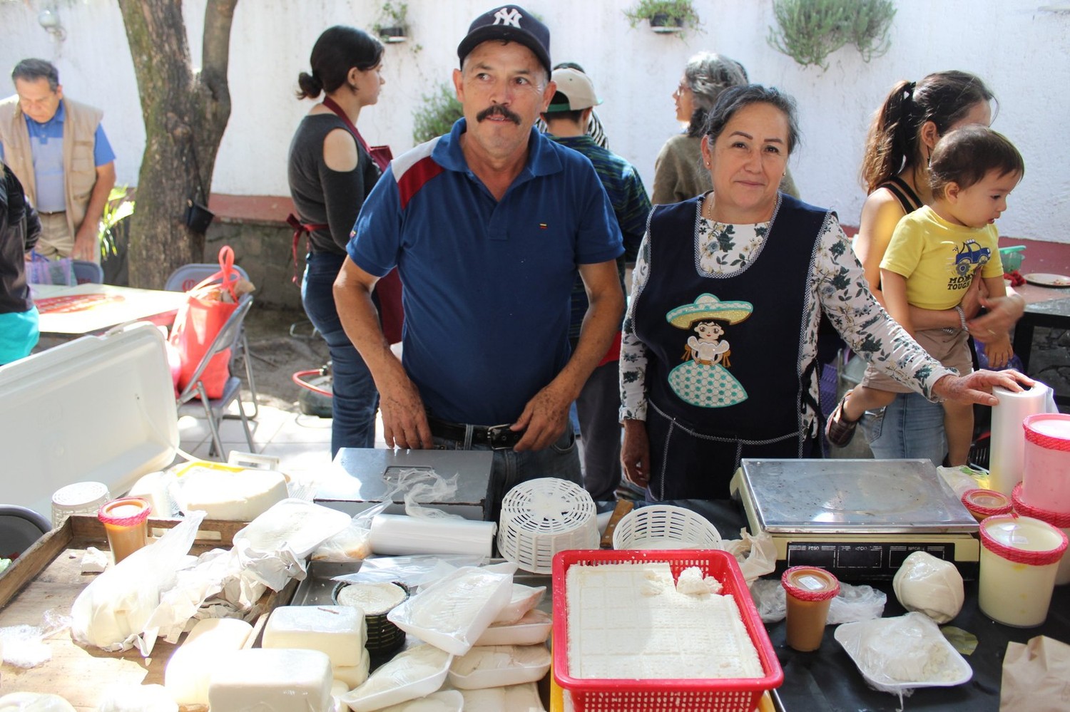 Pareja de productores de Quesos Enciso en su puesto, con quesos frescos, requesón y crema sobre la mesa