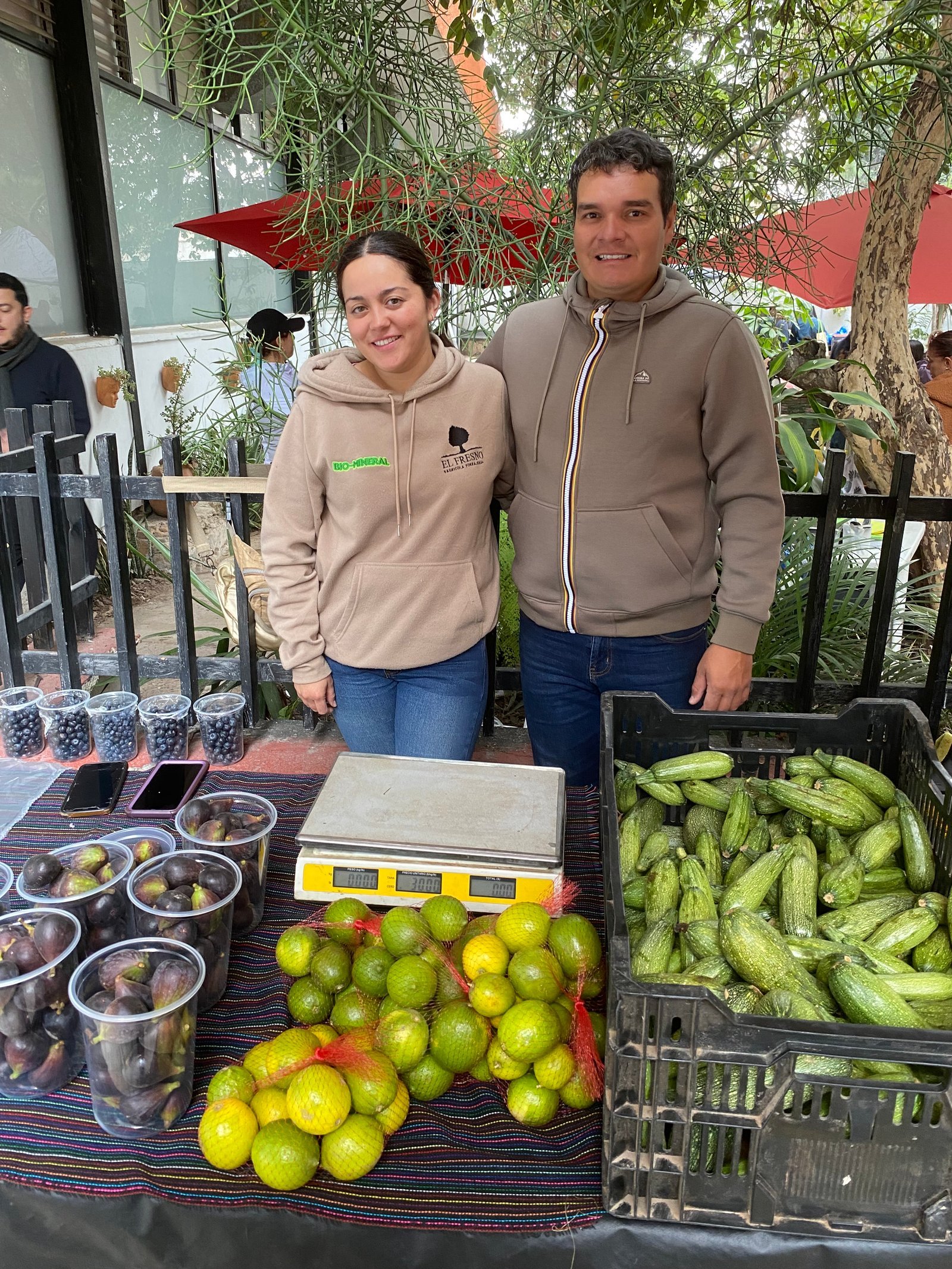 Pareja del equipo de Rancho El Fresno en su puesto, con arándanos, higos, limones y calabacitas sobre la mesa