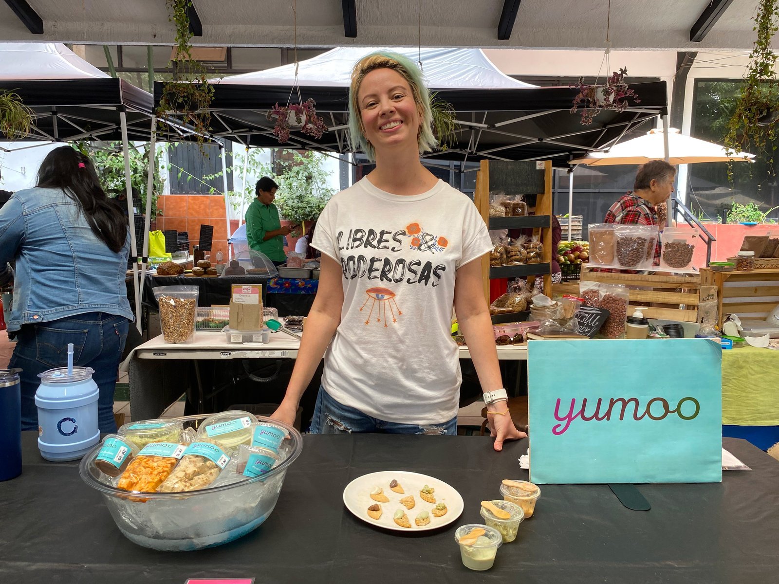 Fundadora de Yumoo en su puesto, junto al letrero de la marca y sus dips proteicos
